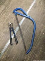Pair of blue-handled bolt cutters alongside a blue metal bow saw with installed blade, displayed on a wooden surface.
