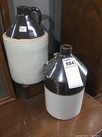 Pair of old stoneware finger jugs, one with intact handle, other with handle broken and small chip. Both about 12 inches tall, glazed brown top and off-white lower portion.