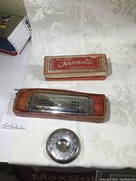 Full view of the chromatic harmonica in its box and the chromatic pitch instrument on a white tablecloth surface.