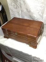 Closed rectangular wooden jewelry box with polished brown finish, curved design, brass drawer and handles.