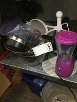 Photo showing small purple blender, weighted paper towel stand, stainless steel bowl, glass bowl, strainer, marble cutting board, and IKEA grater with cookie cutters.