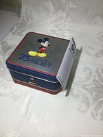 Closed collectible tin box commemorating Disney 75 years with Mickey Mouse, featuring colorful and sketch Mickey images on the top