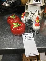 Two pairs of salt and pepper shakers, one tomato-shaped pair and one rooster-shaped pair, displayed on a metal surface with a MaxSold note.
