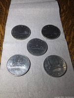 Five vintage Canadian silver dollar coins on white paper towel showing front (obverse) and back (reverse) sides, highlighting details and condition.