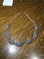 Full view of the necklace laid flat showing the chain and leaf patterned sections