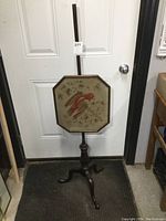 Full view of the Victorian wooden fireplace screen with tripod stand and adjustable post against a door.