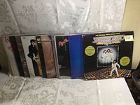Photo showing the full lot of 11 vintage LP records leaning, front visible album is Saturday Night Fever soundtrack.