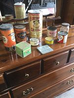 Full grouping of 11 assorted vintage metal tins arranged on wooden surface, showing size and label variations