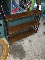 Front view of the walnut wall shelf showing three shelves and carved side details.