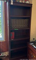 Front view of dark wooden bookcase with some books on one shelf and decorative items on top.