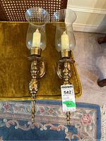 Two brass and glass wall candle sconces placed on gold velvet chair showing front and top views