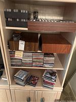 Full view of wooden cabinet with shelves showing neatly stacked cassette tapes in wooden trays and stacks of CD jewel cases.