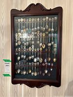Front view of wooden wall-mounted display case containing collector spoons with colorful crests
