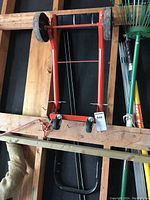 Foldable red metal dolly hung in a wooden garage wall with visible pneumatic and caster wheels.