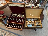 Two open flatware boxes on table showing both silver plate and stainless steel sets