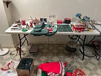 White folding table with various holiday decorations on and around it, showing the entire table and metal legs, placed on a tiled floor.