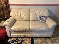 Front view of the cream faux leather loveseat with two removable cushions and the fabric care package placed on the right seat cushion.