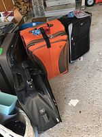 Four pieces of luggage arranged together in a garage setting with some bungee cords visible on top of two suitcases.