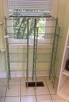 Front view of two green metal plant shelves with ornate scrollwork and multiple horizontal tiers for displays.