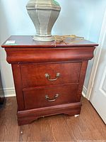 Front view of wood night stand showing two drawers and metal handles with reddish-brown wood finish.