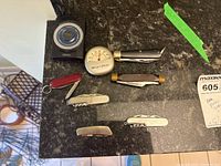 Top view of six folding cutlery pieces with mixed handle materials including wood, brass, and stainless steel alongside two compact timers on dark granite counter.