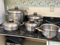 Overview of assortment of stainless steel pots and pans on countertop with bakeware trays underneath