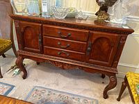 Front view of wood veneer sideboard showing two cabinet doors, three central drawers, carved details on legs and apron.