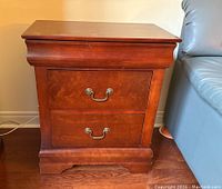 Front view of the wooden side table showing two drawers with metal handles and the polished brown finish.