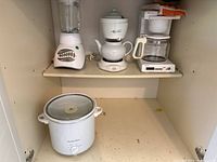 View of all four appliances including the Phillips coffee maker, Proctor Silex slow cooker, Mrs Tea Maker electric tea kettle, and Oster blender arranged on shelves.