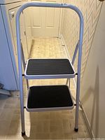 Front view of white folding stepladder with two black rubber steps and upper support handle