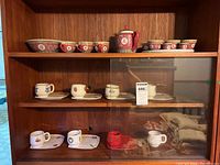 Three shelves with tea sets and teacups with saucers, showing a variety of styles and designs, mostly Chinese-themed with floral and character motifs