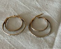 Pair of double hoop 10k gold earrings laying on cloth background showing textured inner hoops and smooth outer hoops with post latch closure.