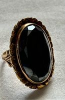 Close-up image of the large oval black faceted stone on the ring from an angle showing the gold setting details.