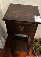 Dark wood antique side table photographed at an angle showing the drawer, wood grain, and scratches on the side and drawer face.