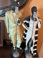 Front view of both musician figurines next to each other, showing the color and details of the figures and microphones.