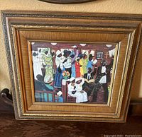 Front view of wood framed colored art print with people in colorful outfits in indoor scene, showing frame and glass condition.
