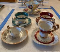 Top view of multiple vintage mini teacups and saucers arranged on table, showing different patterns and colors