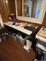 Two white 4-foot folding tables set up against a wood-paneled wall holding various items. Tables show signs of wear and scratches.