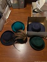 Overview photo of five ladies hats on floor, showing variety of colors and some feather decoration.