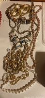 Photo showing multiple long ladies' necklaces including gold-tone metal chain styles, beaded strands with blue stones, faux pearls, and pinkish beads.