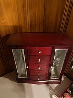 Wooden jewelry cabinet with closed drawers and glass doors against a wood-paneled background, highlighting overall condition and design.