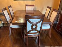 Dining table with six matching chairs arranged around it on hardwood floor, showing front and side views of the set.