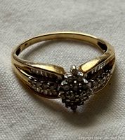 Close-up photo showing the yellow gold ring with cluster of stones and stones along the band on white fabric background.