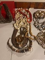 Photo showing variety of costume necklaces including white bead, red bead, gold tone choker and bracelets.