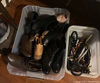 Plastic bin with multiple pairs of ladies size 8.5 footwear including boots and sandals, and a separate bin containing assorted leather and fabric belts in mostly black and brown shades.