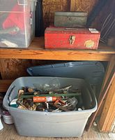 Two vintage metal toolboxes and a large gray plastic tote filled with assorted tools and supplies, visible on a wooden shelf in a barn.