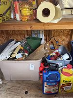 Two plastic totes filled with assorted garden tools and supplies including a rusty hand saw, garden chemicals like Bayer Home Defense and Preen Weed Preventer, and various hand tools.
