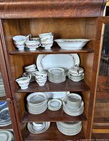 China set arranged on wooden shelves showing cups, plates, saucers, and bowls with floral garland pattern.