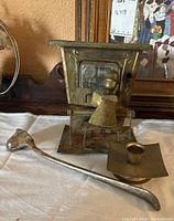 Vintage brass candleholder resembling a stove, silver-plated candle snuffer, and small brass dish on white surface.