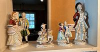 Front view of four vintage porcelain figurines on display shelf under natural light